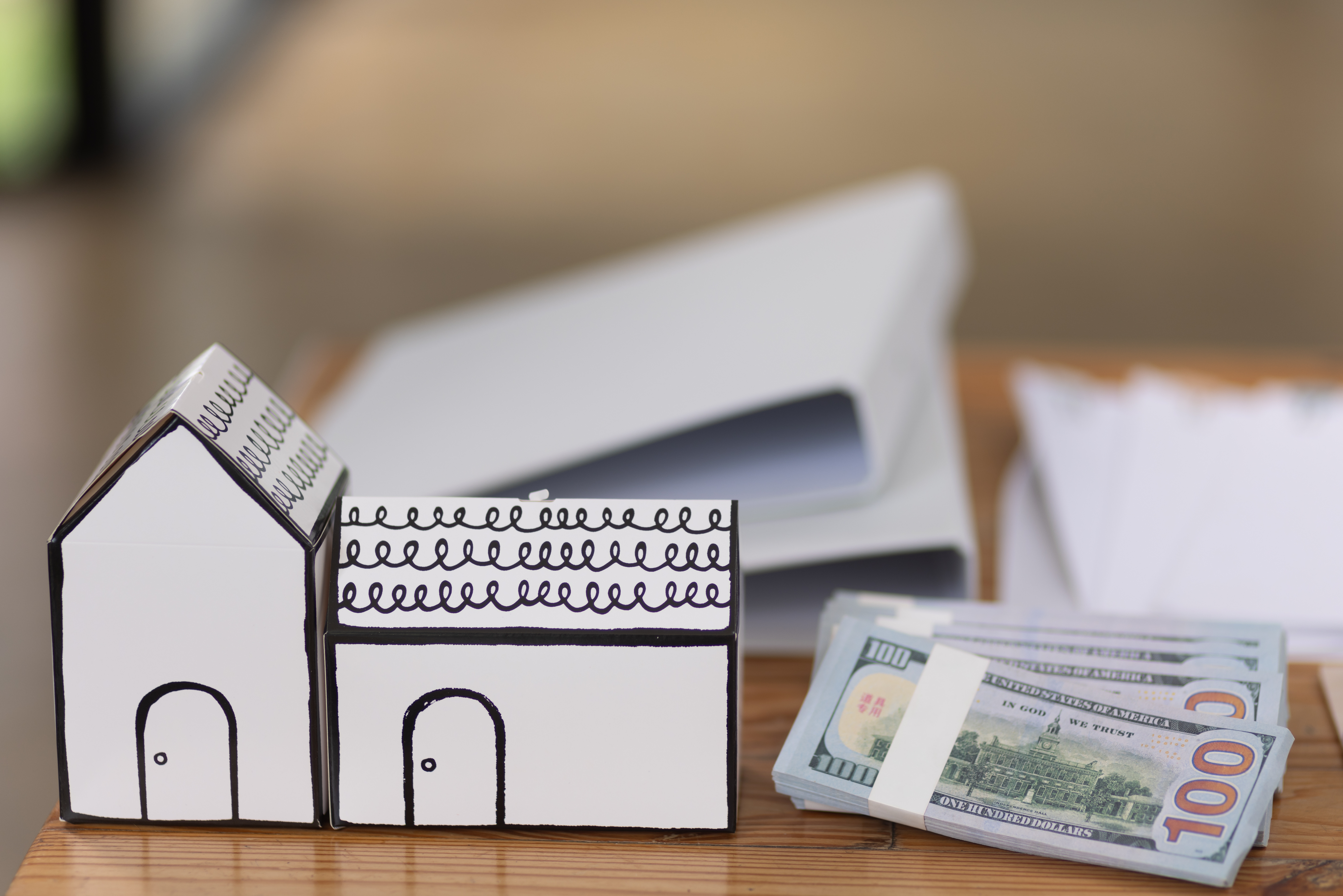 Cash home sale concept with house models and hundred dollar bills on desk